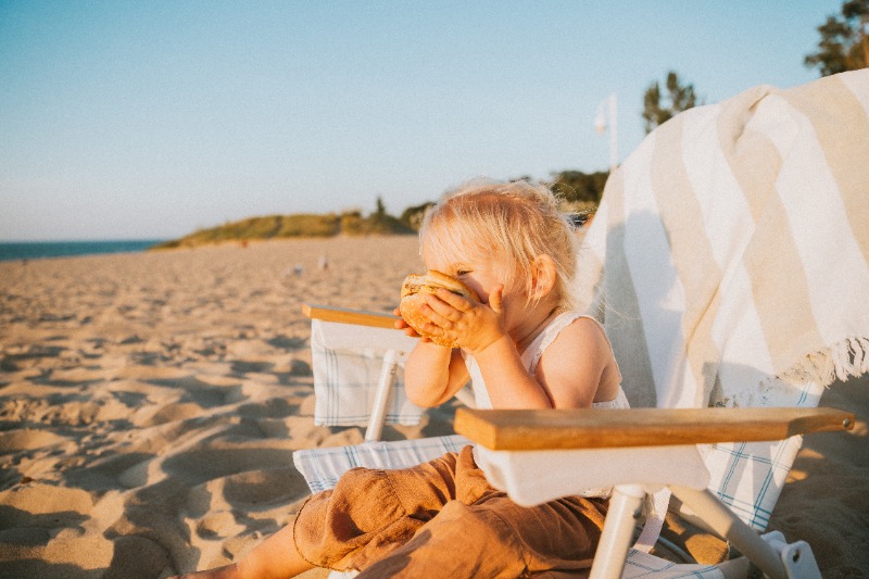 Lake Michigan Getaway: A young girl cutely holds a hamburger while lounging at the beach on Lake Michigan.